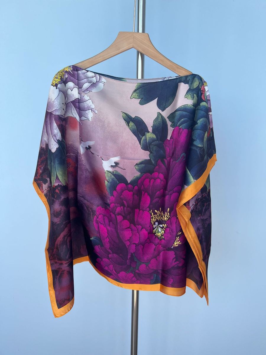 Faux-silk printed hijab scarf hanging on a wooden hanger, orange edge with floral pattern